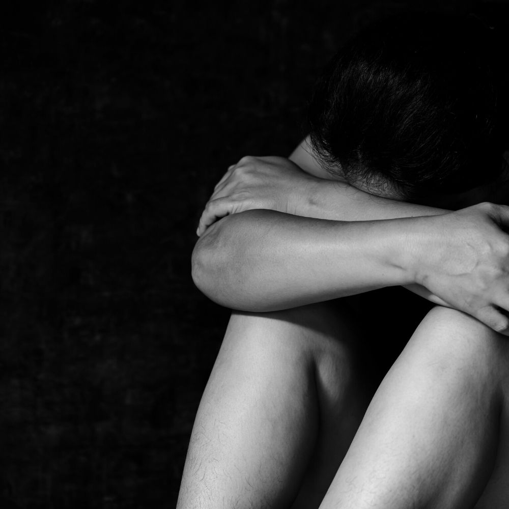 black and white image of a person with their head in their arms