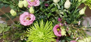 A vibrant bouquet featuring green chrysanthemums, pink lisianthus flowers, and surrounding greenery. This bloom arrangement is lush and colorful, showcasing a wild variety of textures with buds and leaves.