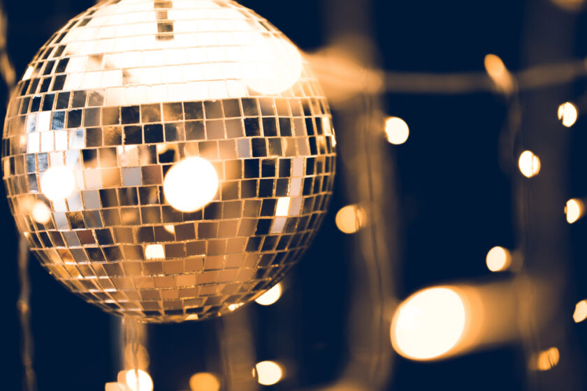 Close-up of a shimmering disco ball reflecting warm lights, set against a dark background with blurry golden bokeh. The mirrored tiles create a vibrant and lively atmosphere, capturing the essence of a festive night.