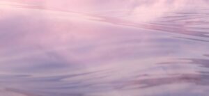 A serene view of a pink sunset reflecting on rippling water. The soft hues and gentle waves create a tranquil and peaceful atmosphere.