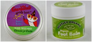 The image shows two balms. On the left is Gwdihw Goody Hoo hand balm featuring an owl in a wizard hat. On the right is Bentley Organic Foot Balm, labeled with tea tree and peppermint. Both have white containers and colorful labels.