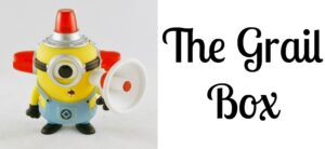 A toy figure resembling a Minion with a megaphone and a siren hat stands next to the text The Grail Box in a playful font. The Minion wears blue overalls and has one eye.