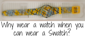 A colorful Swatch watch with a zigzag pattern, featuring blue, yellow, and gray colors. It is placed in a transparent case. Below, text reads, Why wear a watch when you can wear a Swatch?.