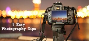 A camera on a tripod is focused on a city skyline at night with bright bokeh lights in the background. The cameras screen shows a clear view of the buildings. Text on the left reads, 5 Easy Photography Tips.