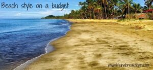 Sandy beach with gentle waves, lined with palm trees under a clear blue sky. Text on the image reads Beach style on a budget with a website link in the corner.
