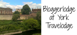 View of a historic building and lush greenery under a blue sky. On the right, text reads Bloggerlodge at Travelodge York, perfectly capturing the charm and allure of this enchanting destination.