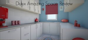 Modern kitchen with white cabinets, blue walls, a red coffee machine, and a red window blind. A small rug is on the floor, and various kitchen items are placed on the counters. The text Dulux Amazing Space: Review is at the top of the image.