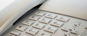 Close-up of a grey office telephone keypad. The keypad includes numeric buttons and letters, arranged in a standard layout. The image focuses on the top section, highlighting the buttons with numbers 1 to 9 and special characters.