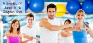 A group of people exercising together in a gym, all wearing athletic clothing and smiling. Text overlay reads 5 Benefits Of Joining A No Obligation Gym. Blue exercise balls are visible in the background.
