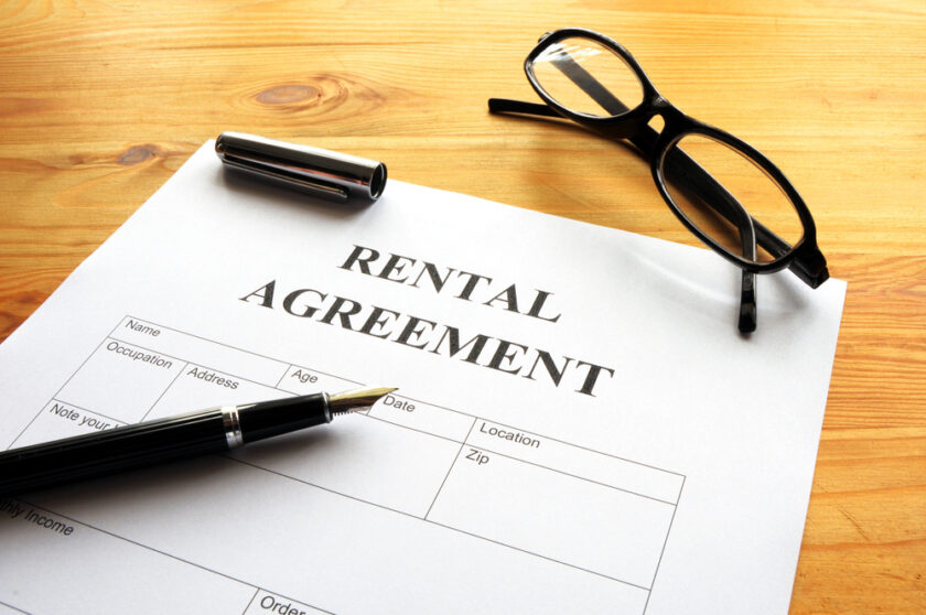 A rental agreement form on a wooden table with a black pen and eyeglasses placed beside it, ready to be filled out.