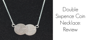 A necklace featuring two overlapping sixpence coins on a silver chain, displayed against a black background. The text on the right reads Double Sixpence Coin Necklace: Review.