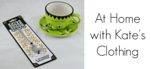 A decorative green teacup and saucer featuring a face design sits beside a packaged novelty sugar spoon. The package reads SUGAR SPOON - A STIRRING REMINDER, capturing the essence of Kates Clothing at home.