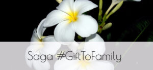 White flowers with yellow centers against a dark background. The text reads Saga #GiftToFamily in the foreground.