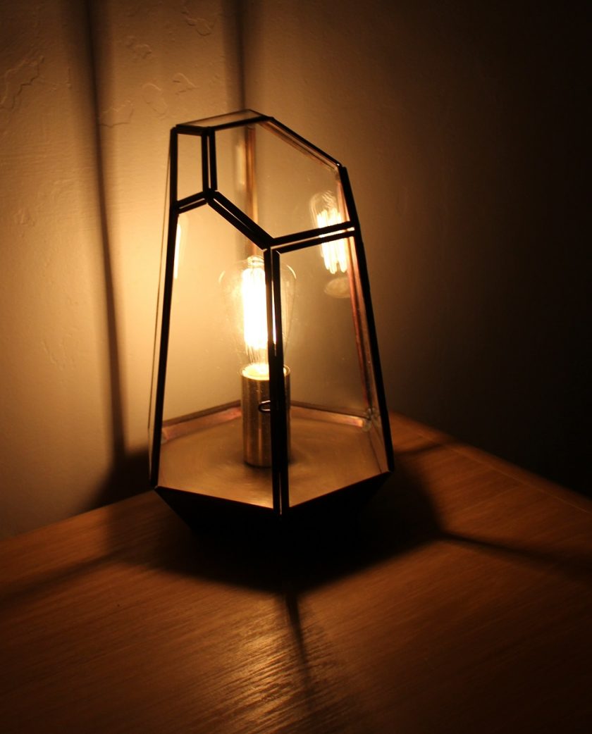 Litecraft Terrarium Candle Lantern Table Lamp - Antique Brass with edison screw filament squirrel cage light bulb. Lamp lit up in semi darkness, picture taken from the front of the lamp