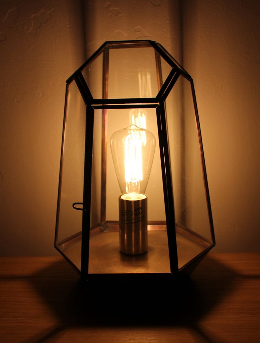 Litecraft Terrarium Candle Lantern Table Lamp - Antique Brass with edison screw filament squirrel cage light bulb. Lamp lit up in semi darkness, picture taken from the front of the lamp