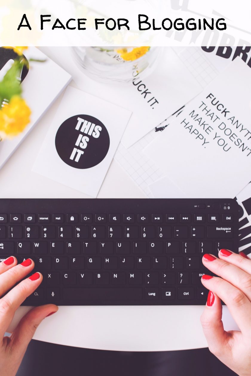 Hands with red nail polish typing on a black keyboard. Nearby lies a notebook and papers with motivational quotes. Yellow flowers and a coaster inscribed with This is it are on the table. Text at the top reads, A Face for Blogging.