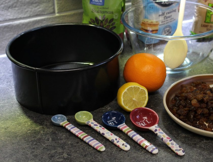 Christmas at Debenhams - Christmas cake making, cake tin, measuring spoons, lemon, orange, mixing bowl and dried fruit - close up of bowl and spoons