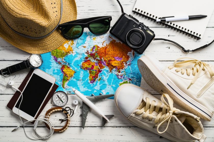 Image of a map, shoes, phone, mini plane, sunglasses and other accessories you may need on holiday.