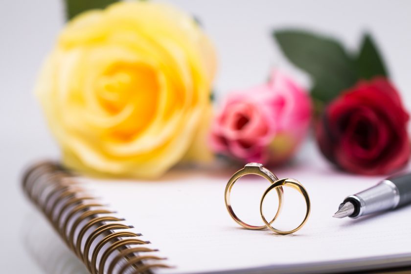 Wedding Rings sat on a paper pad with a yellow rose and other flowers in the background