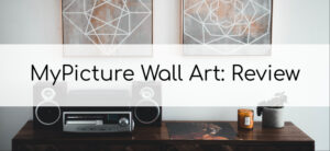 A wooden table with a stereo system, a candle, and a plant. Two geometric wall art pieces hang above. The text MyPicture Wall Art: Review is centered over the image.