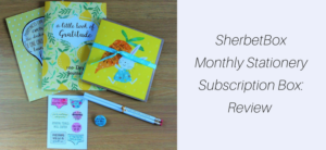 Image of a SherbetBox stationery subscription set featuring a 100 Days of Gratitude journal, greeting cards adorned with heart and fruit designs, motivational stickers, a sleek pen, and a charming button badge. Text on the right reads: SherbetBox Monthly Stationery Subscription Box: Review.
