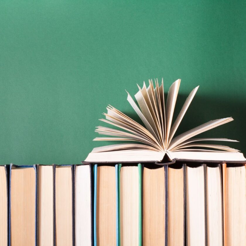 open book on top of other books with a green backdrop