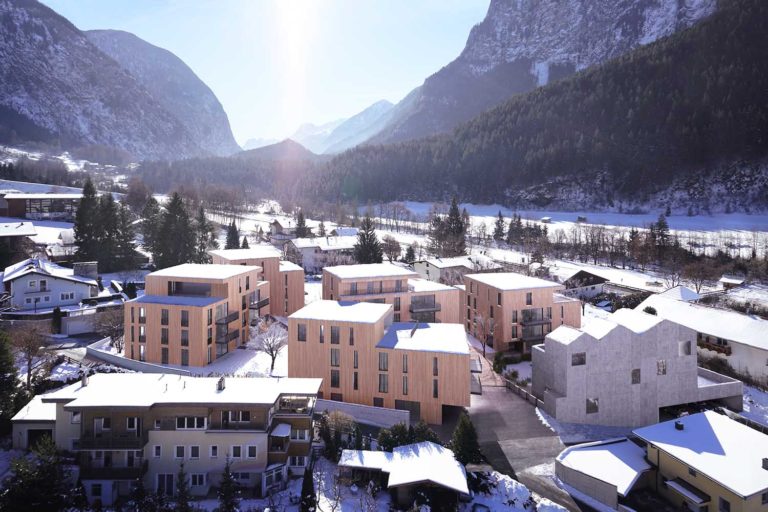 Aerial view of a snowy mountain village featuring modern wooden and stone buildings. Majestic mountains surround the village, and sunlight filters through, casting a serene glow over the scene.