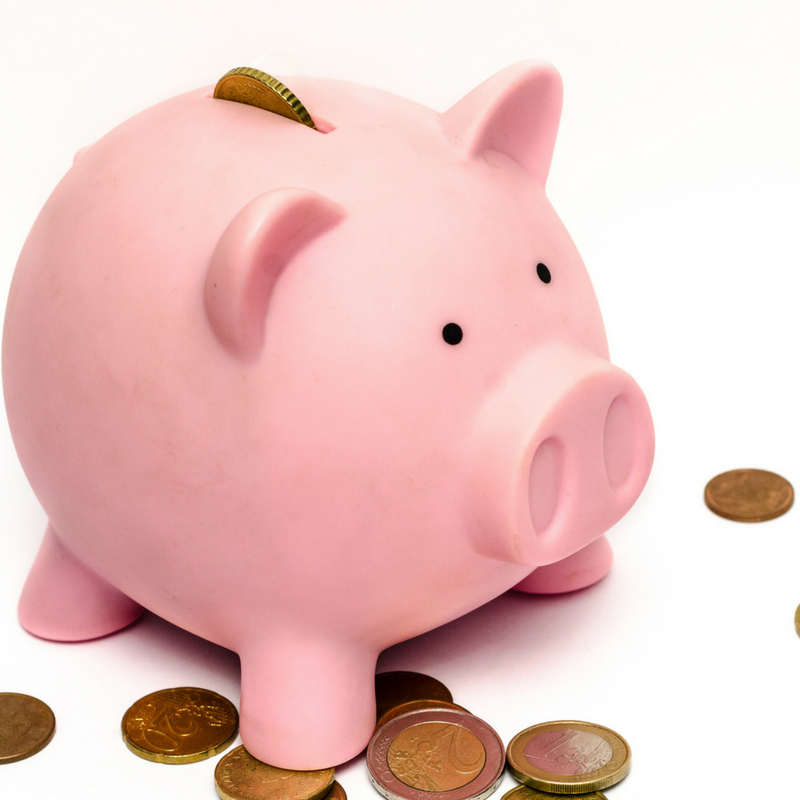 A pink piggy bank with a coin inserted into its slot is surrounded by a few scattered coins on a white background.
