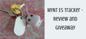 A set of keys includes a yellow key cover and a white MYNT ES tracker on a pink and gray textured surface. A small gray character charm is also attached. Text on the right reads MYNT ES tracker - Review and Giveaway.