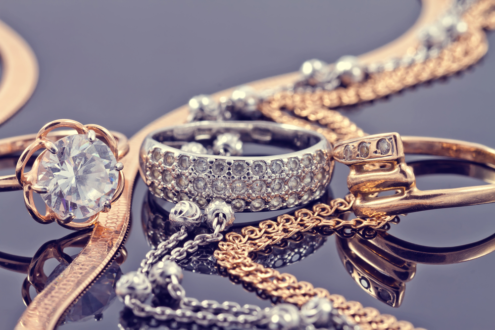 Gold, silver rings and chains of different styles are lying together on the reflecting surface