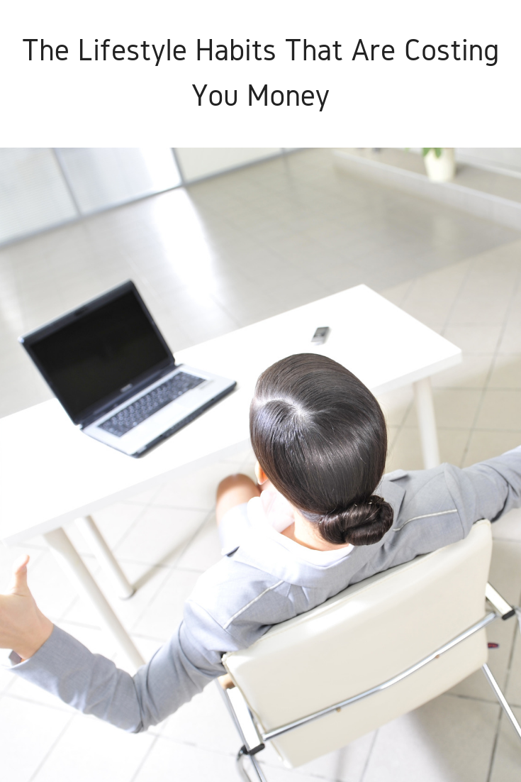 A person sitting at a desk with an open laptop, arms outstretched in a questioning pose. The text above reads, The Lifestyle Habits That Are Costing You Money. The setting is a bright, modern office.