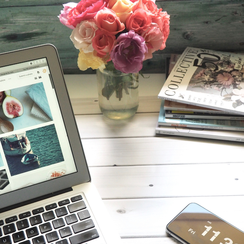 computer and phone with flowers and magazines in the background