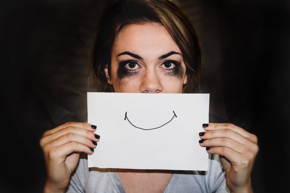 person holding a piece of paper with a smile drawn on, mascara smudged around the eyes