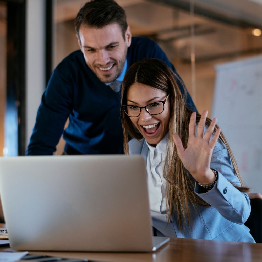 two people looking happy in front of a computer one with a hand up