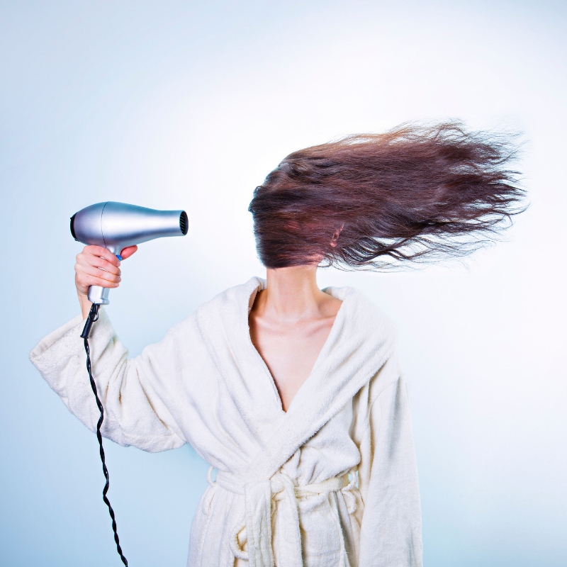 picture of someone holding a blowdryer and there hair blowing across their face