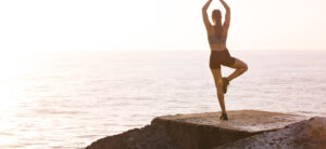 person stood in a yoga pose looking out at the sea