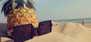 pineapple and sunglasses on the sand with sea in the background