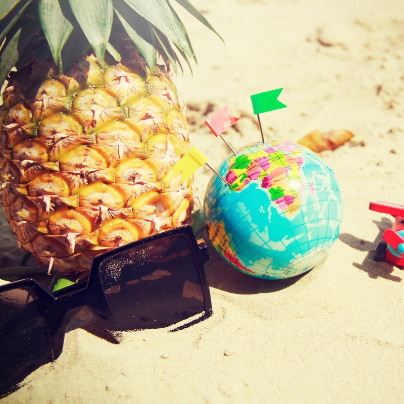 pineapple, sunglasses and globe on the sand