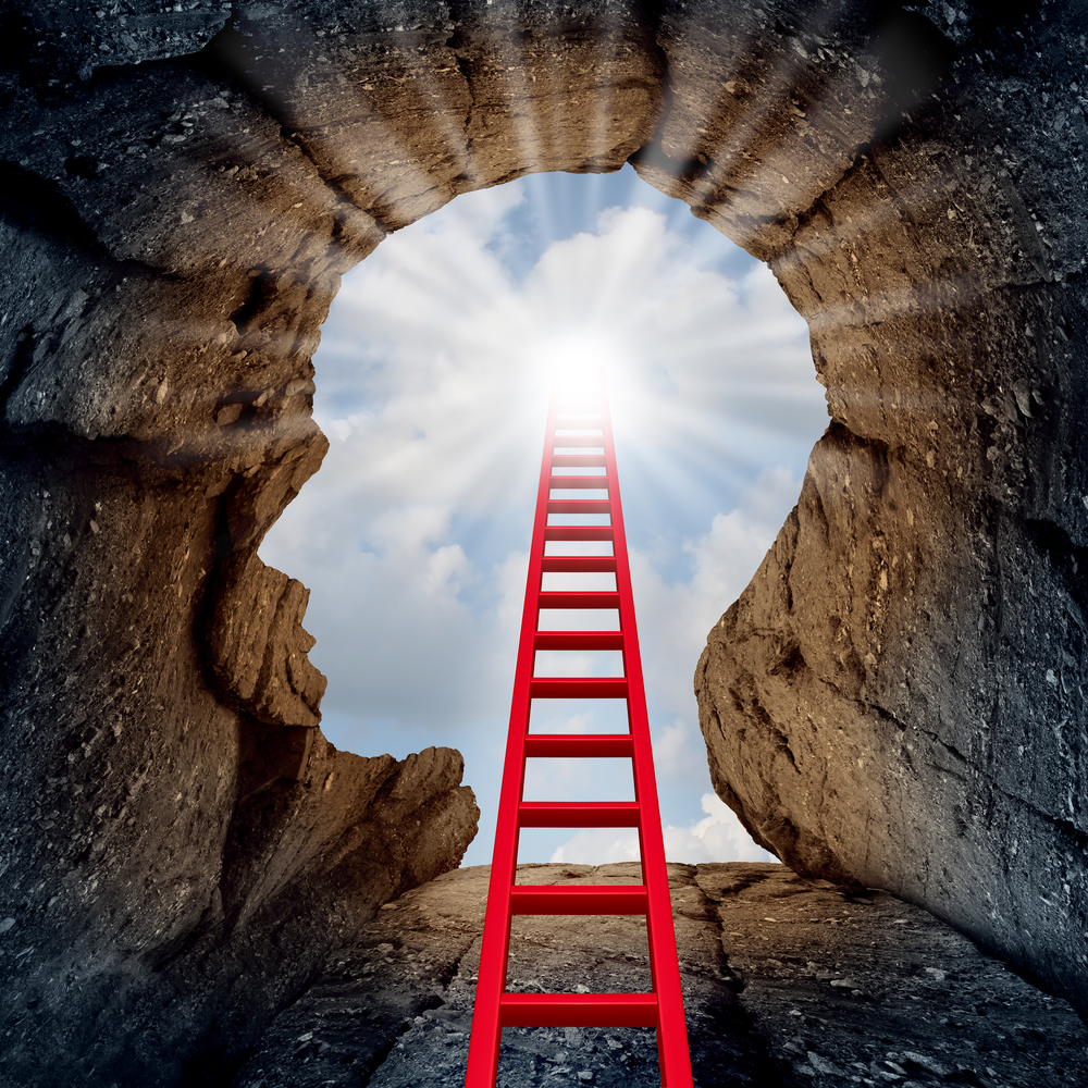 Concept of open mind as a a deep mountain cliff shaped as a human head with a ladder leading to the outside towards a glowing sun.