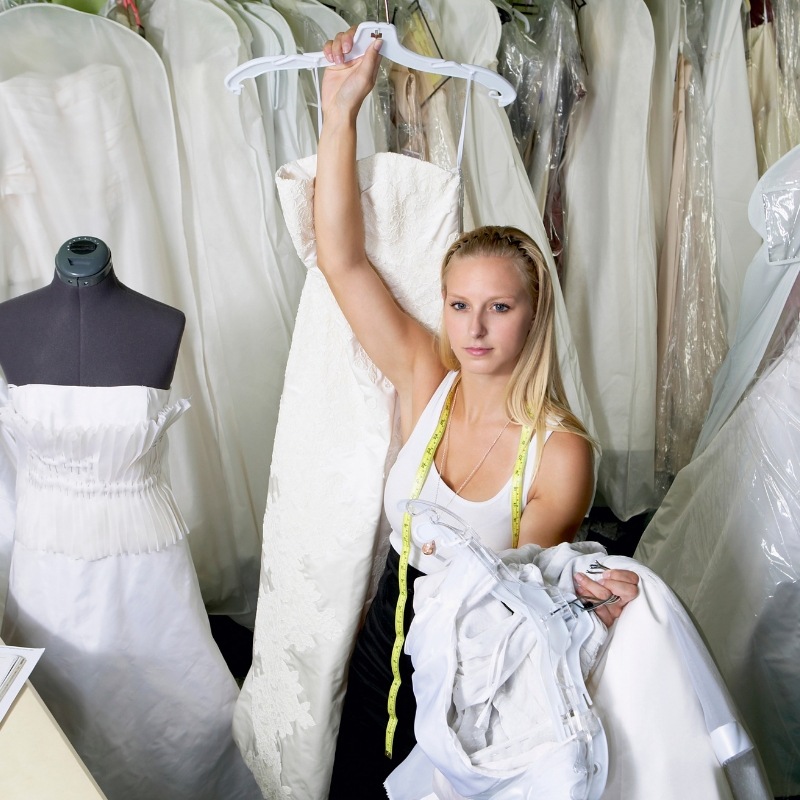 lady holding a wedding dress with tape measure around her neck