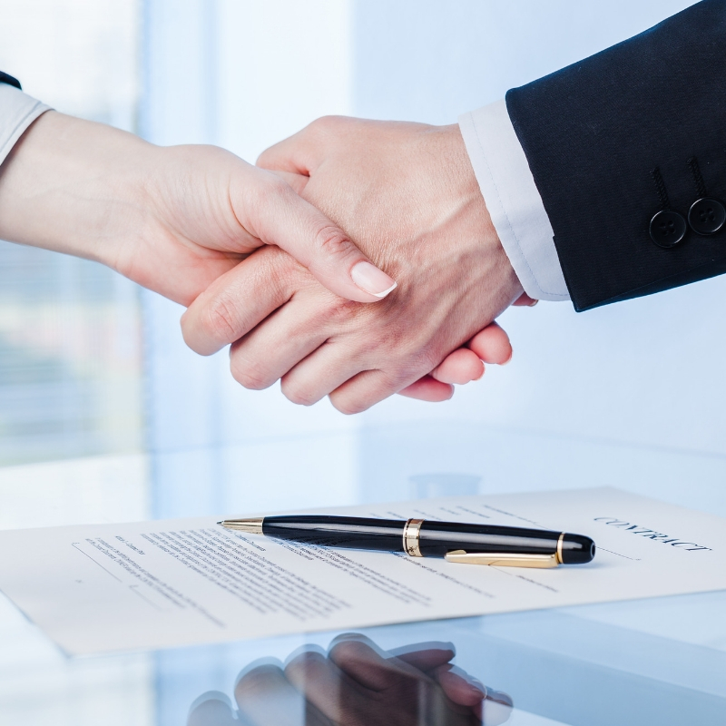 two people shaking hands over a signed contract