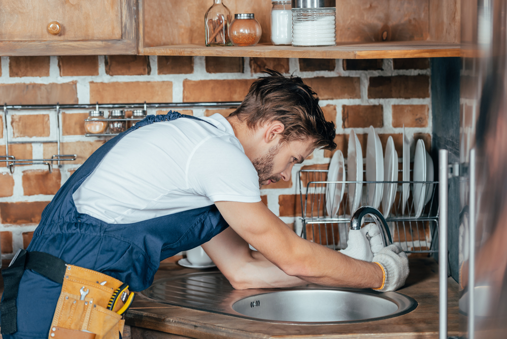 Side view of young handyman repairing sink in kitchen