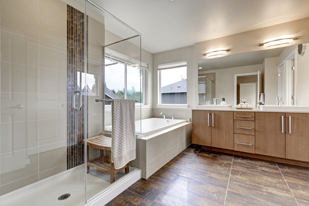 White modern bathroom interior in brand-new house. Double sink vanity with large mirror, walk-in shower, white bath tub and brown tile floor. Northwest, USA