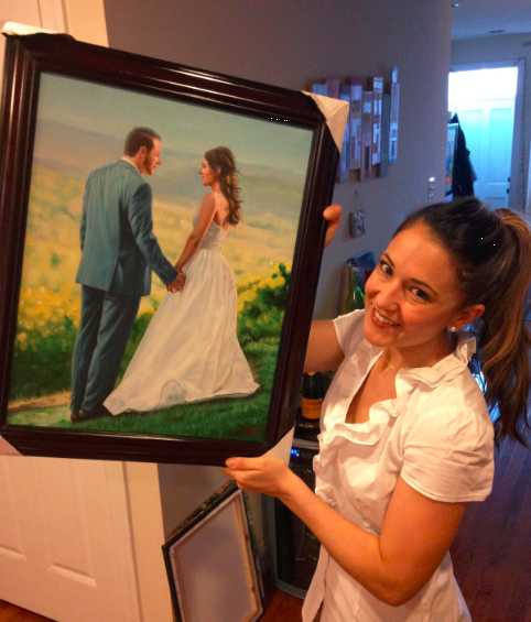 Woman shows off the gift she received: a customized oil painting from a photo taken on her wedding day, depicting her and her husband side by side, holding hands.