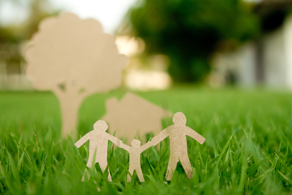 Paper cut of family with house and tree on fresh spring green grass