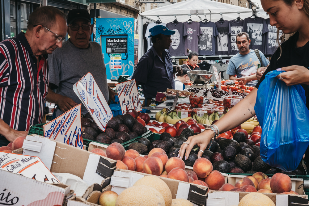 London, UK - July 22, 2018: Woman buying fresh fruits in Brick Lane, London. The street is the heart of the London's Bangladeshi-Sylheti community and is famous for its many curry houses.
