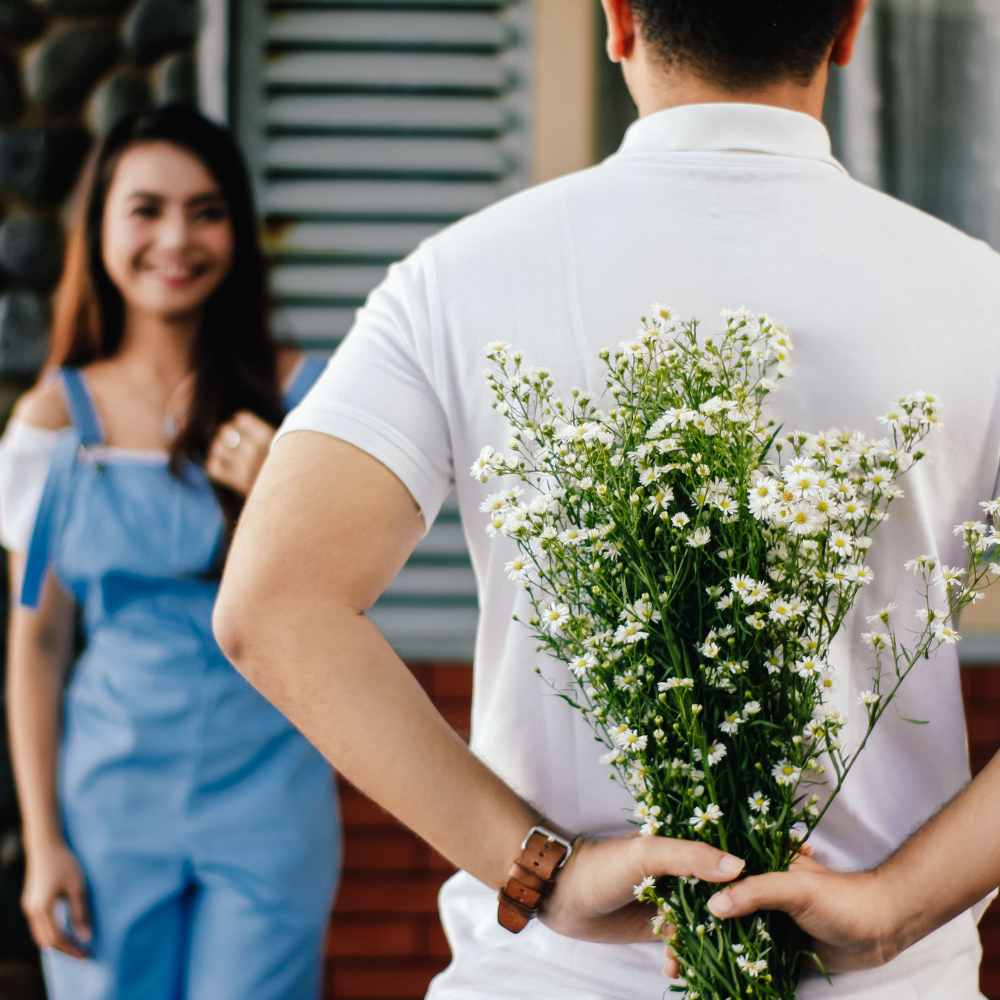 man hiding flowers behind his back with women in front of him