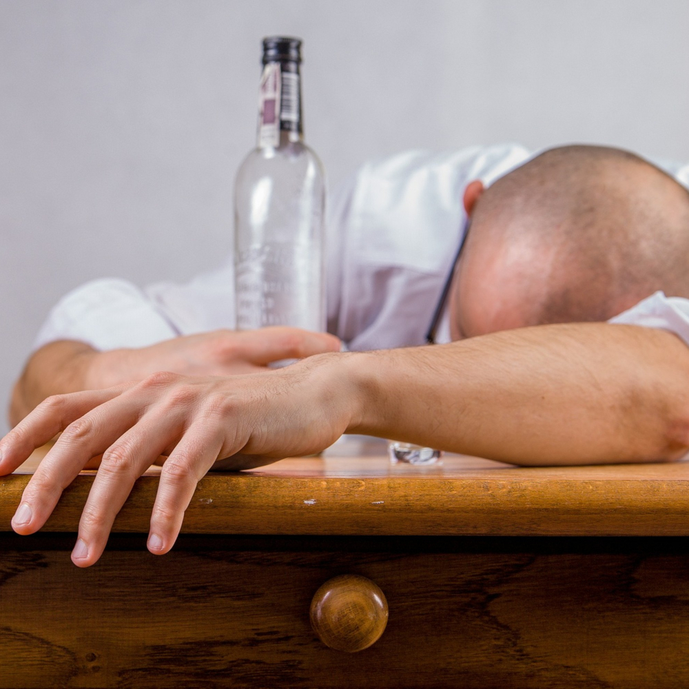person with their head on a table and empty bottle