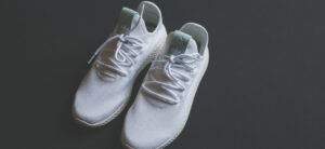 A pair of white athletic sneakers with green inner lining and visible branding on the tongue, positioned on a dark background. The laces are untied.