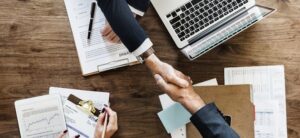 two people shaking hands at a business meeting with paperwork around them